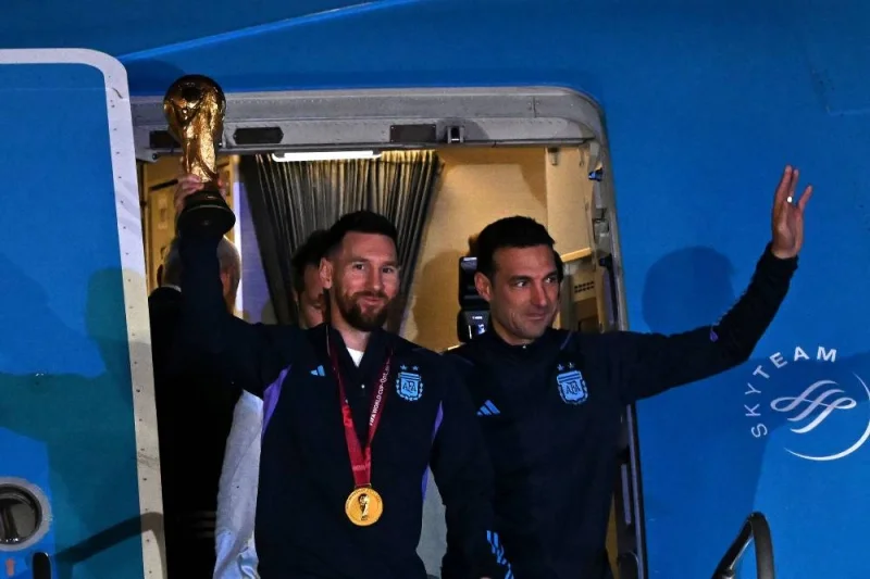 Argentina&#039;s captain and forward Lionel Messi holds the FIFA World Cup Trophy alongside Argentina&#039;s coach Lionel Scaloni as they step off a plane upon arrival at Ezeiza International Airport after winning the Qatar 2022 World Cup tournament. (AFP)