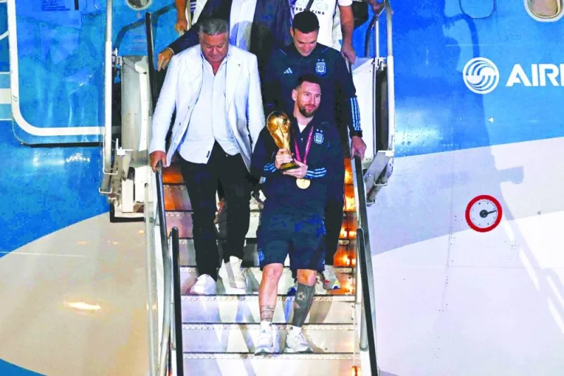 Argentina’s captain Lionel Messi (centre) holds the World Cup Trophy as he steps off a plane upon arrival at Ezeiza International Airport after winning the Qatar 2022 World Cup in Ezeiza, Argentina, yesterday. (AFP)