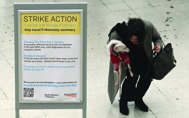 A traveller holds a dog next to an information board announcing the rail strike action at Waterloo Station in London.