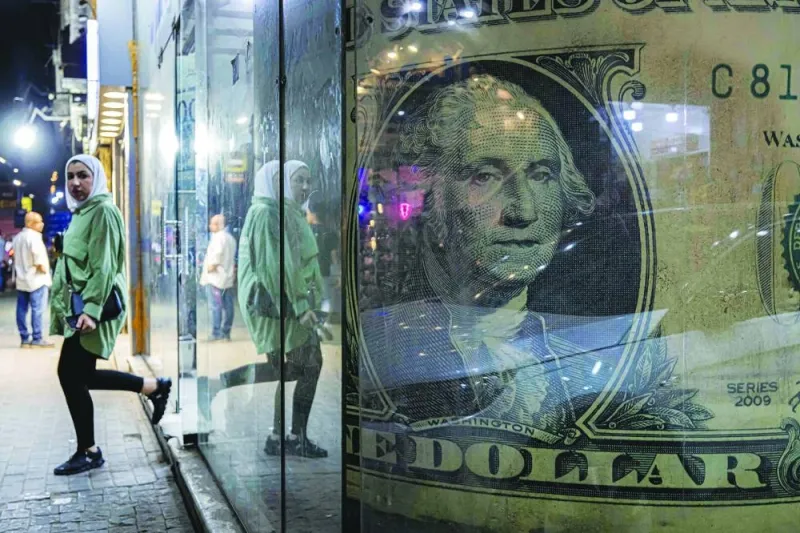 A woman walks out of a currency exchange shop displaying a giant US dollar banknote in the Zamalek district of Egypt’s capital Cairo. Egypt let the pound weaken twice in 2022, eventually clinching a $3bn loan from the International Monetary Fund with a pledge in October to adopt a flexible exchange-rate.