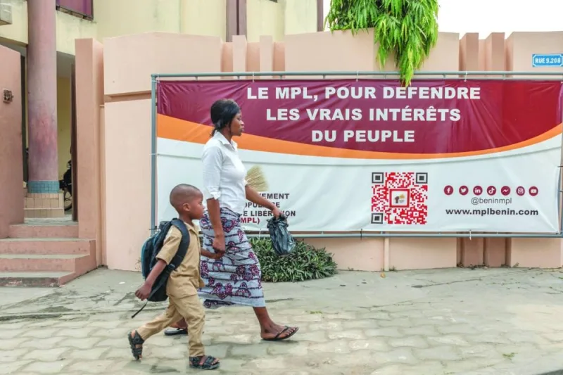 A woman with her child walks past a banner of the Popular Liberation Movement at their headquarters in Cotonou.