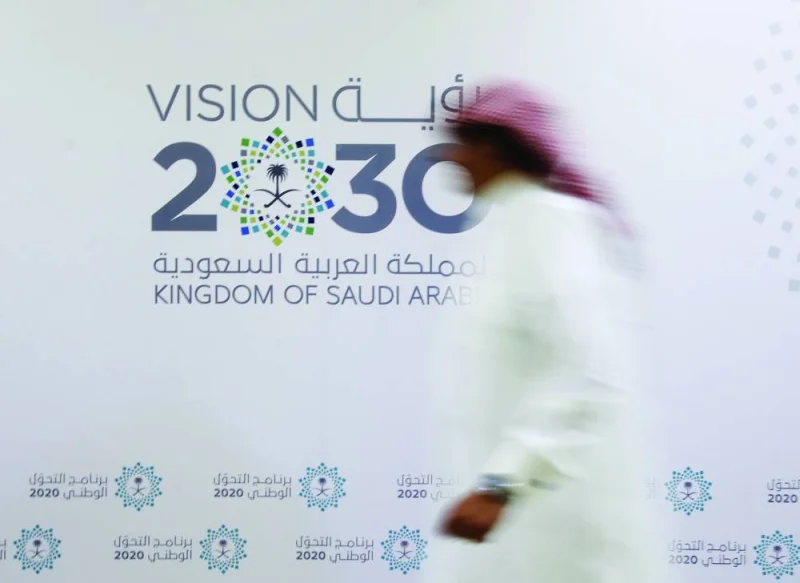 A Saudi man walks past the logo of Vision 2030 in Jeddah (file). While corporate lending is seen picking up due to projects linked to the 'Vision 2030' agenda to diversify away from oil, 'funding availability will likely be a constraint for the first time in a while,' S&P said in its Saudi Banking Sector 2023 Outlook.