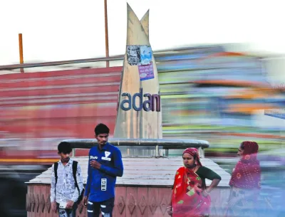 People wait to cross a road in front of the logo of the Adani Group installed at a roundabout on the ring road in Ahmedabad, India. In a sign of just how prohibitively expensive any attempted debt financing for group firms could now be, the yield on an Adani Green Energy Ltd bond spiralled over 36% last week.