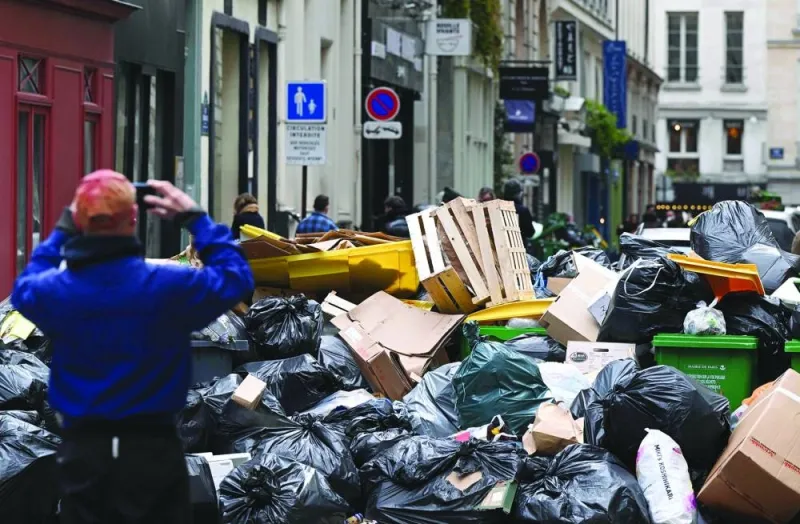A pedestrian takes a picture of household waste containers in a street of Paris, which have been piling up since collectors went on strike against the French government’s proposed pensions reform.