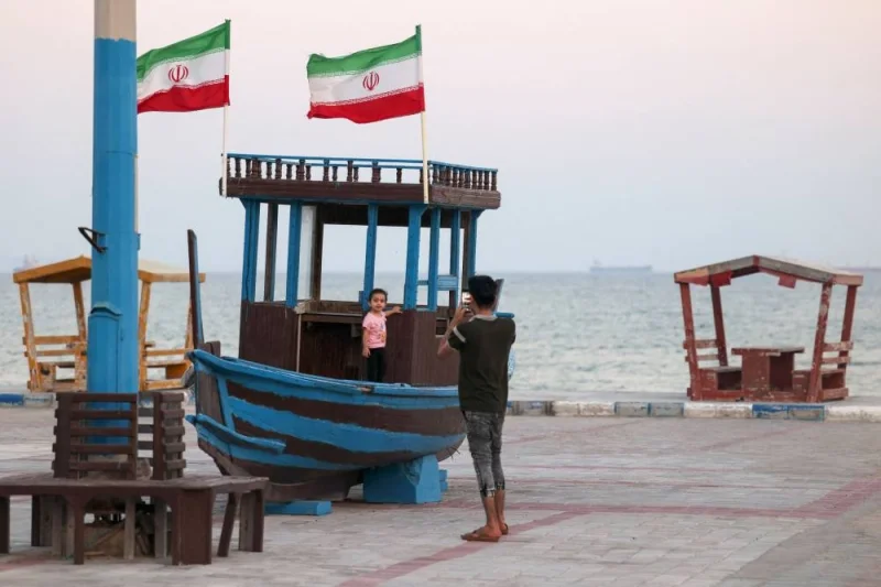 People on a seaside promenade as shipping vessels sail past Iran's Gulf island of Qeshm.