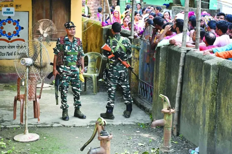 Paramilitary soldiers stand guard as people queue at a polling station to cast their votes on the outskirts of Kolkata, yesterday.