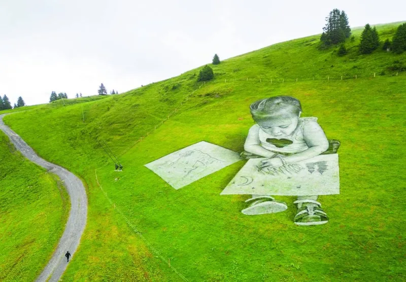 
Right: Swiss-French artist SAYPE walks towards his land art painting, depicting a child drawing, at the Col de Bretaye in Villars-sur-Ollon, Switzerland. 