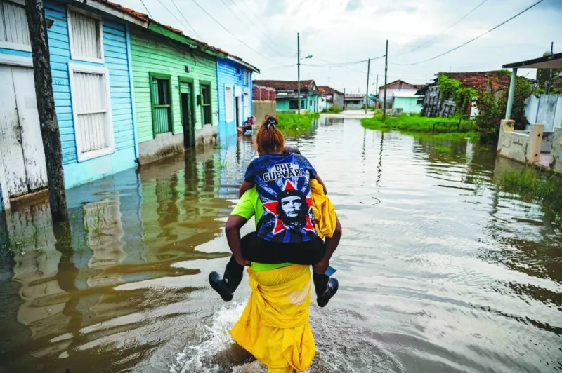 
Left: A man carries a woman as he wades through the water in a flooded area of Batabano, Mayabeque Province, Cuba. 