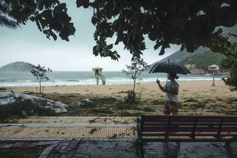 A woman films a beach covered with tree branches in the aftermath of Typhoon Saola at a coastal village in Hong Kong on Saturday.