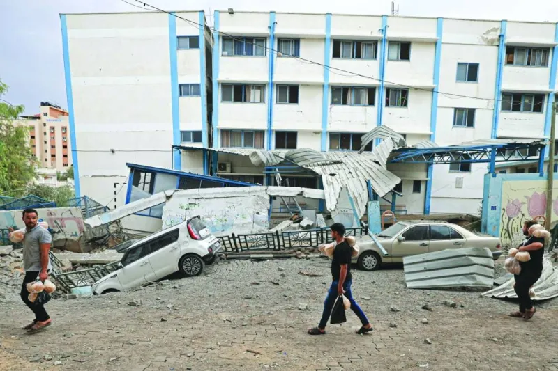 Palestinian men carrying bread walk past damaged cars and a crater in front of a school run by the United Nations Relief and Works Agency for Palestine refugees (UNRWA) following Israeli airstrikes targeting Gaza City on Monday.