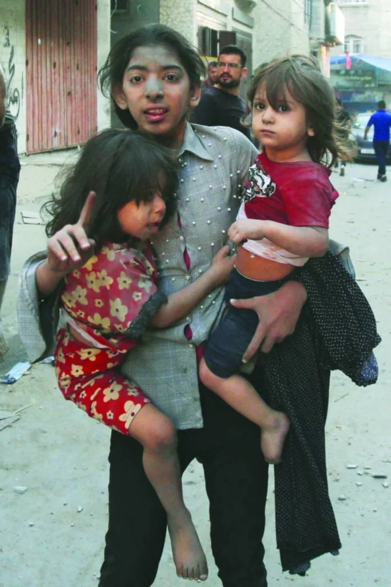 
A girl holds two children as she stands on a street in Gaza City following an Israeli military strike. 