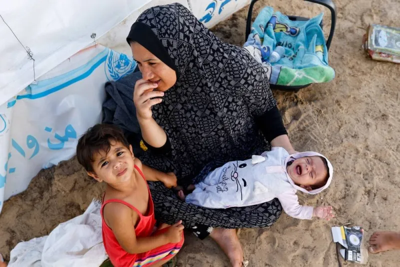 A woman sits with children as displaced Palestinians, who fled their houses amid Israeli strikes, take shelter at a tent camp at a United Nations-run centre, in Khan Younis in the southern Gaza Strip, on Monday. REUTERS