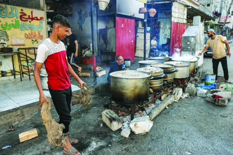 Men carry logs of wood to be used in fires heating up large cooking pots outdoors along a street in Rafah in the southern Gaza Strip, on Tuesday.