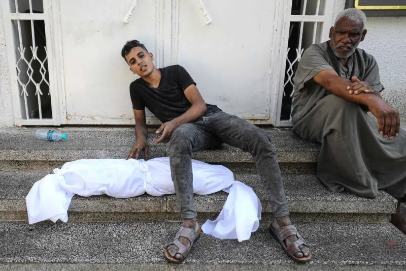 A Palestinian man sits on a step with the body of a child wrapped in a shroud next to him, outside a hospital following Israel&#039;s bombardment of Gaza City&#039;s eastern suburb of Shujaiya on Saturday. AFP
