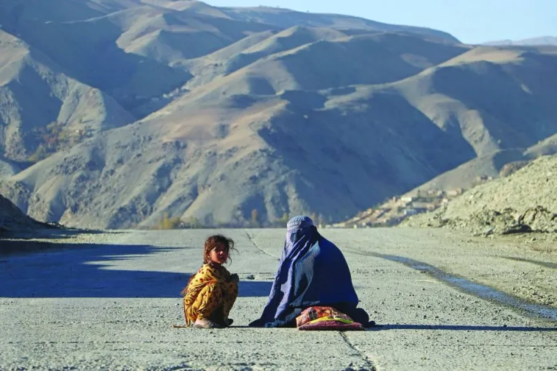 TOPSHOT - An Afghan burqa-clad woman sits beside a girl, as they look for alms along a street in the Fayzabad district of Badakhshan province on November 16, 2023. (Photo by OMER ABRAR / AFP)