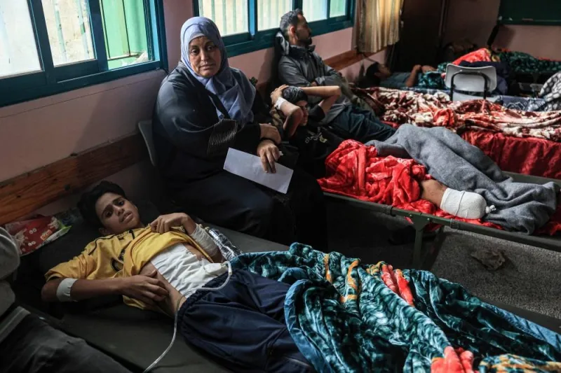 Sahar Awad, 49, sits between her injured nephews, Mossaab, 14,(R) and his cousin Abboud, 12, in a classroom at the Ras Al-Naqoura school in Khan Yunis in the southern Gaza Strip, after being transferred from the Indonesian Hospital in the north, on November 22. AFP