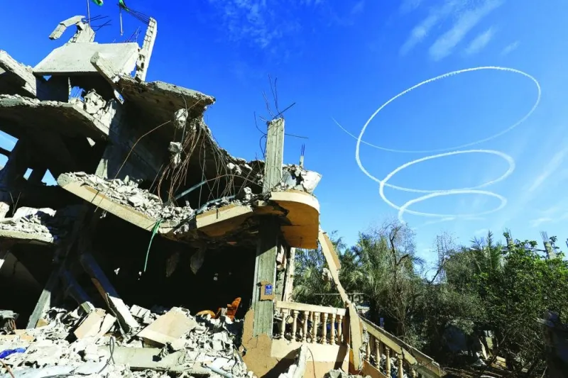 Israeli aircraft leave trails in the sky above the ruins of houses destroyed in Israeli strikes on Khan Younis in southern Gaza Strip during the conflict, amid a temporary truce between Hamas and Israel.