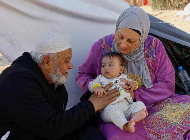 Abedulkader Sarsoor, a retired plastic surgeon, sits next to his wife and grandchild, as displaced Palestinians, who fled their houses due to Israeli strikes, shelter in a tent camp near the border with Egypt, in Rafah in the southern Gaza Strip, on Monday. REUTERS