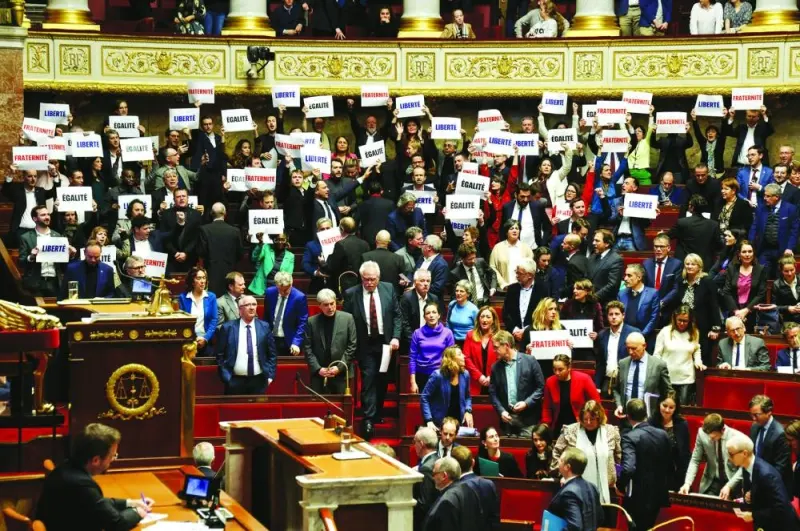 Left-wing coalition NUPES members of parliament hold signs reading “Liberte”, “Egalite”, “fraternite” French for ‘liberty, equality, fraternity’, the national motto of France, following the vote and the approval of the draft law to control immigration at the French National Assembly in Paris on Wednesday. (AFP)