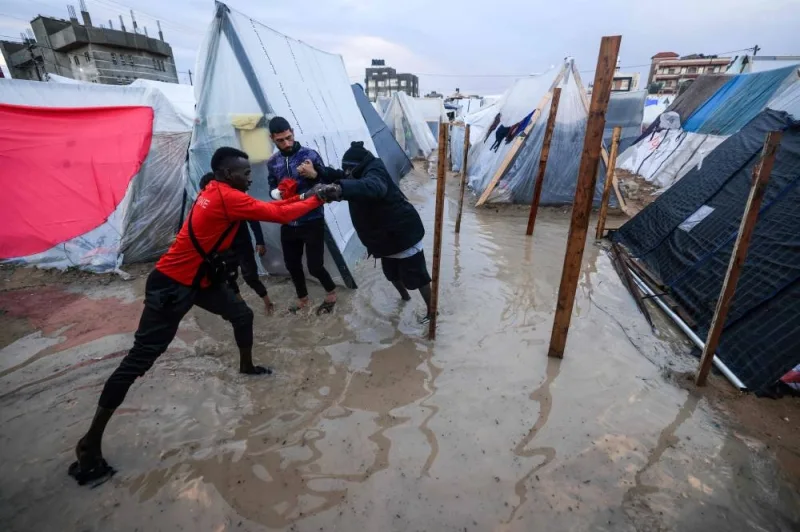 A displaced Palestinian man helps a woman to find her way amid tents flooded by heavy rain, at a makeshift camp set up by people who fled the ongoing battles, in Rafah in the southern Gaza Strip on Saturday. AFP