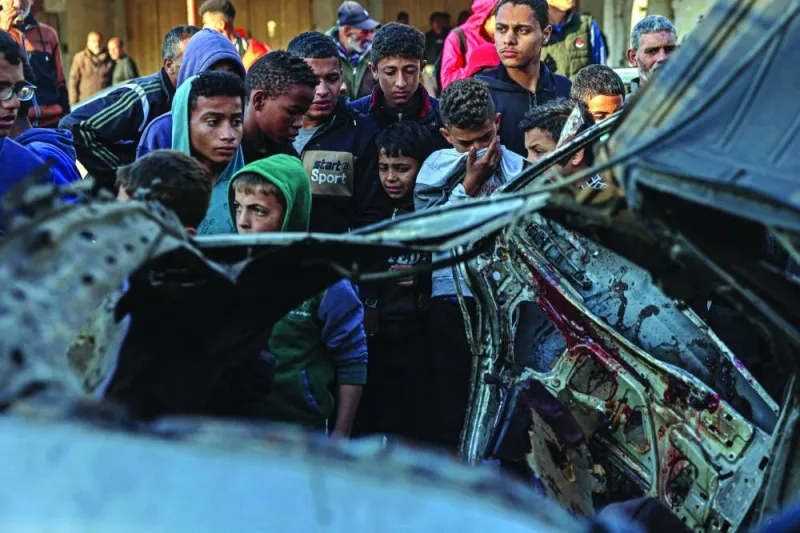 Onlookers gather around a car that was destroyed in an Israeli raid in Rafah Tuesday.