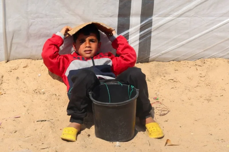 Displaced Palestinian boy, who fled his house due to Israeli strikes, uses a piece of cardboard to protect himself from the sun, at a tent camp, near the border with Egypt, in Rafah in the southern Gaza Strip, Sunday. REUTERS