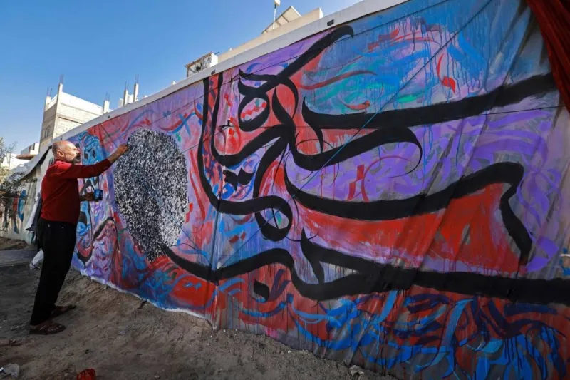 Palestinian artist Basil al-Maqousi draws calligraphy on the tent of displaced people along a street in Rafah.