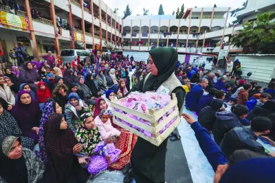 A woman distributes sweets to displaced Palestinians as they attend a special morning prayer to start the Eid al-Fitr festival, at a school-turned-shelter in Rafah, southern Gaza Strip.