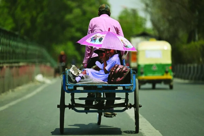 Children shelter from the sun under an umbrella while travelling in the back of a bicycle cart during a hot summer day in New Delhi on Thursday.