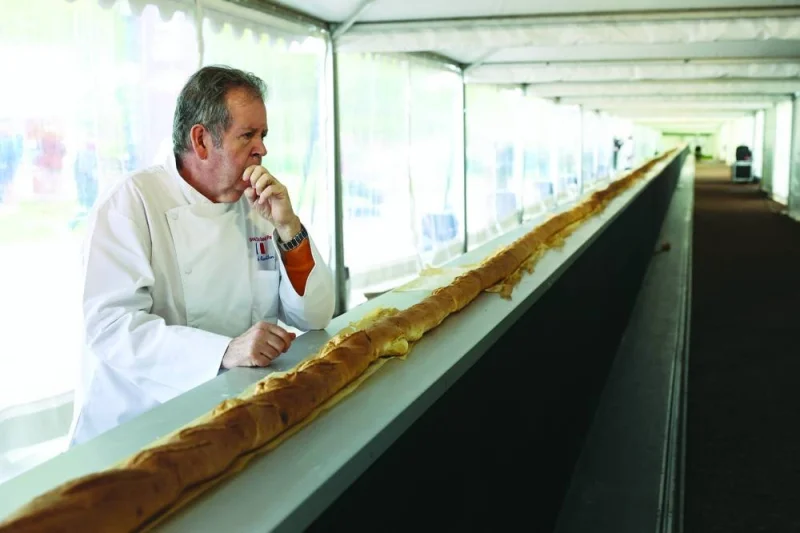 A French baker stands near the baguette as it comes out of a large rotating oven in an attempt to beat the world record for the longest baguette during the Suresnes Baguette Show in Suresnes near Paris, France, May 5, 2024. REUTERS/Stephanie Lecocq