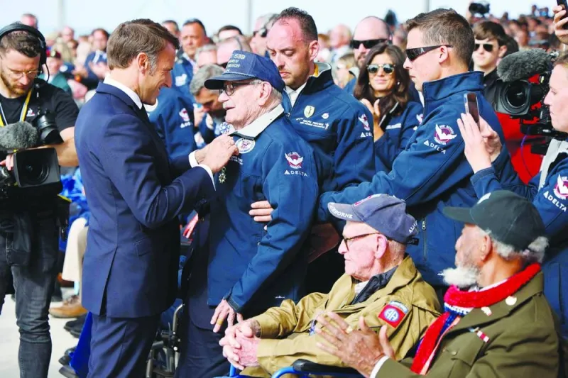 France's President Emmanuel Macron (L) awards US WWII veterans Dick Rung (2ndL), Joseph Miller (seated C) and Arlester Brown (seated Front R) with the Legion of Honour during the International commemorative ceremony at Omaha Beach marking the 80th anniversary of the World War II "D-Day" Allied landings in Normandy, in Saint-Laurent-sur-Mer, in northwestern France, on June 6, 2024. The D-Day ceremonies on June 6 this year mark the 80th anniversary since the launch of 'Operation Overlord', a vast military operation by Allied forces in Normandy, which turned the tide of World War II, eventually leading to the liberation of occupied France and the end of the war against Nazi Germany. (Photo by Ludovic MARIN / AFP)