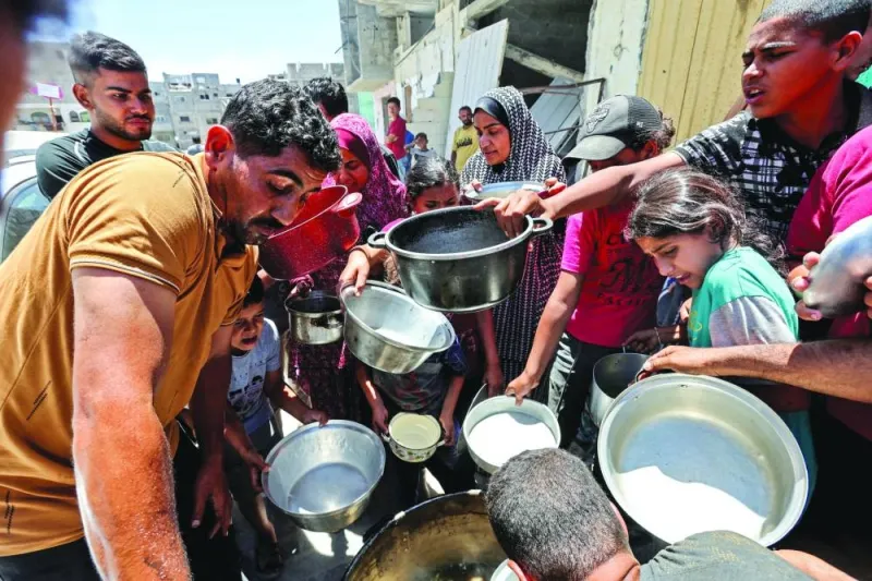 
File photo shows Palestinians gathering to receive food cooked by a charity kitchen near houses destroyed in the Israeli military offensive, in Khan Younis in the southern Gaza Strip. 