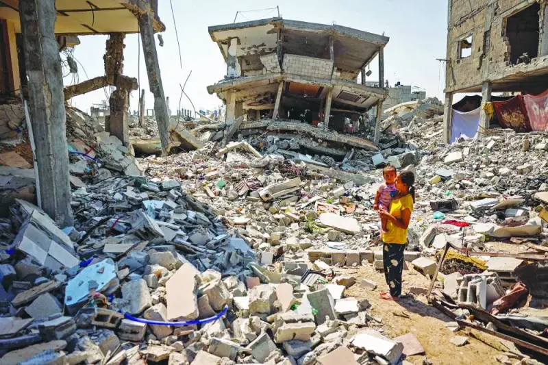  A woman stands holding a child surrounded by the rubble of buildings destroyed during Israeli bombardment in Khan Yunis on the southern Gaza Strip yesterday
