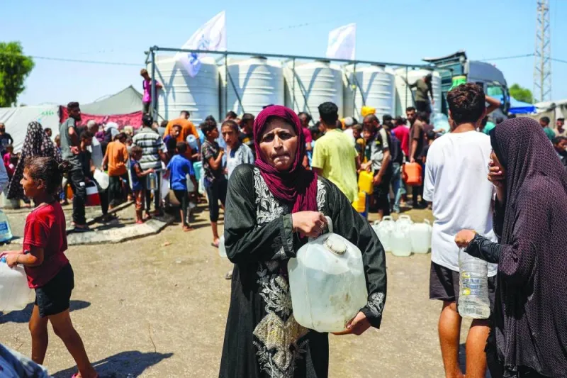 A woman walks with a water container after filling up with others from a truck loaded with water cisterns in Rafah in the southern Gaza Strip, yesterday.