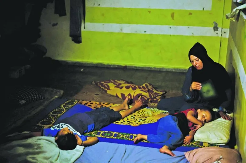 A displaced Palestinian woman, Amal Nsair, fans her children as they sleep in a school where they shelter, during hot weather and power cut, amid the Israel-Hamas conflict, in Khan Younis in the southern Gaza Strip.