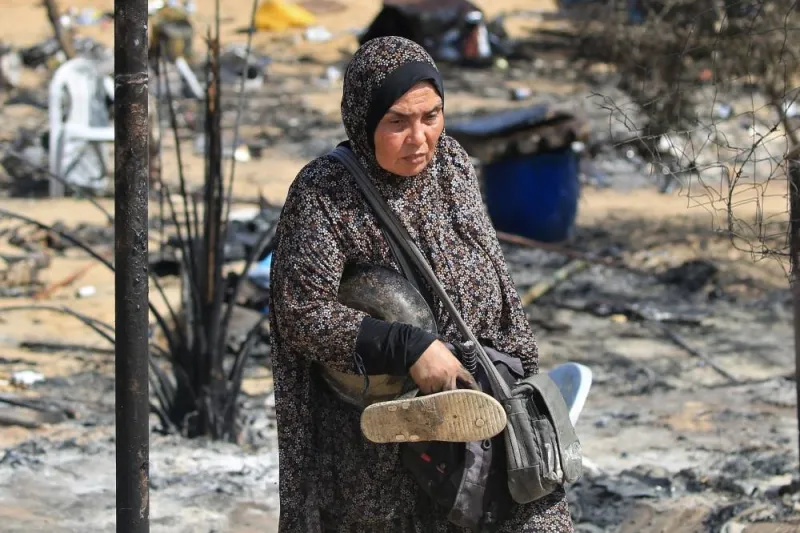 A woman carries salvaged items following an Israeli raid in Rafah on the southern Gaza Strip, on Saturday on a road damaged by Israeli bulldozers. AFP