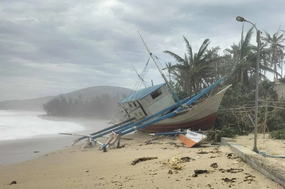 A fishing boat is seen washed ashore in Calayan island, Cagayan province on September 23, 2025, a day after Super Typhoon Ragasa hit the island. Ragasa had already toppled trees, torn the roofs off buildings and killed at least two people in a landslide while lashing the northern Philippines, where thousands sought shelter in schools and evacuation centres. (Photo by Cristy Gaffud / AFP)