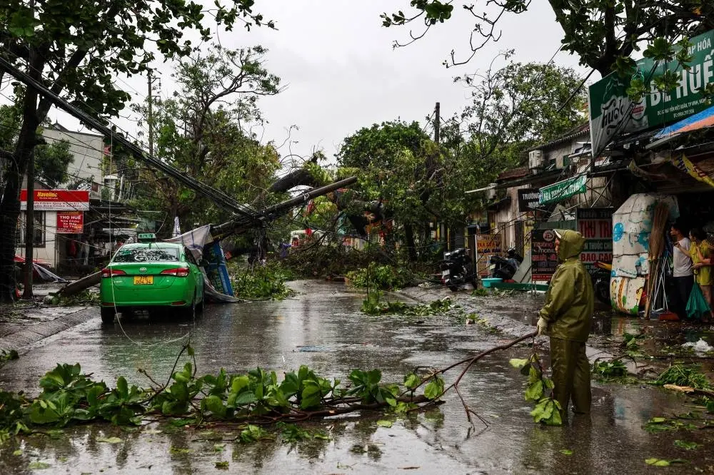 People watch as workers remove fallen trees and electric polls from a road after Typhoon Bualoi makes landfall in Nghe An province, Vietnam, on Monday. REUTERS