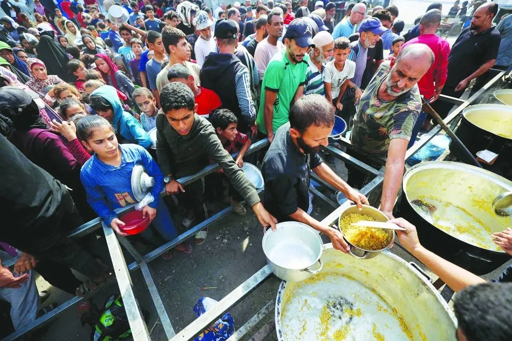 Displayed Palestinians wait for a food portion at a shelter where families have been living, in Nuseirat in the central of Gaza Strip, yesterday.