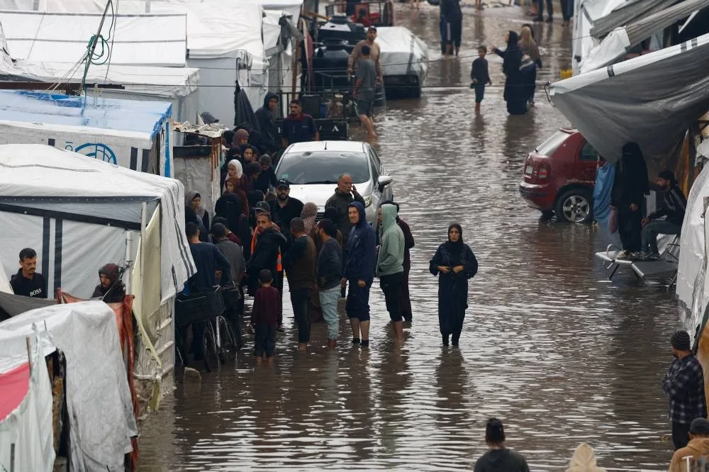 Displaced Palestinians gather next to tents in a flooded area, during a rainy day in Gaza City, November 25, 2025. REUTERS