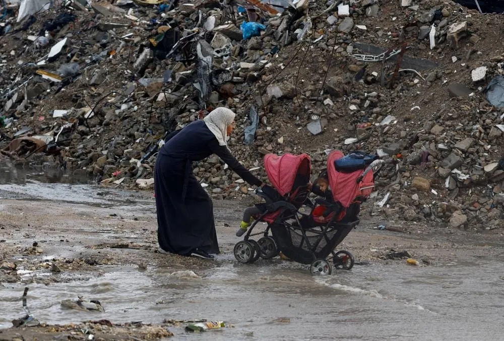A Palestinian woman pulls a stroller with children, next to piles of rubble, during a rainy day in Gaza City, November 25, 2025. REUTERS