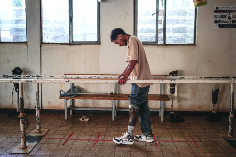 Yosef Debasu, 19, who was injured by a landmine explosion while driving his tuk-tuk in Merawi around August-September 2024, performs rehabilitation exercises with his prosthetic limb while holding parallel bars inside the exercise room of the Bahir Dar Physical Rehabilitation Center.