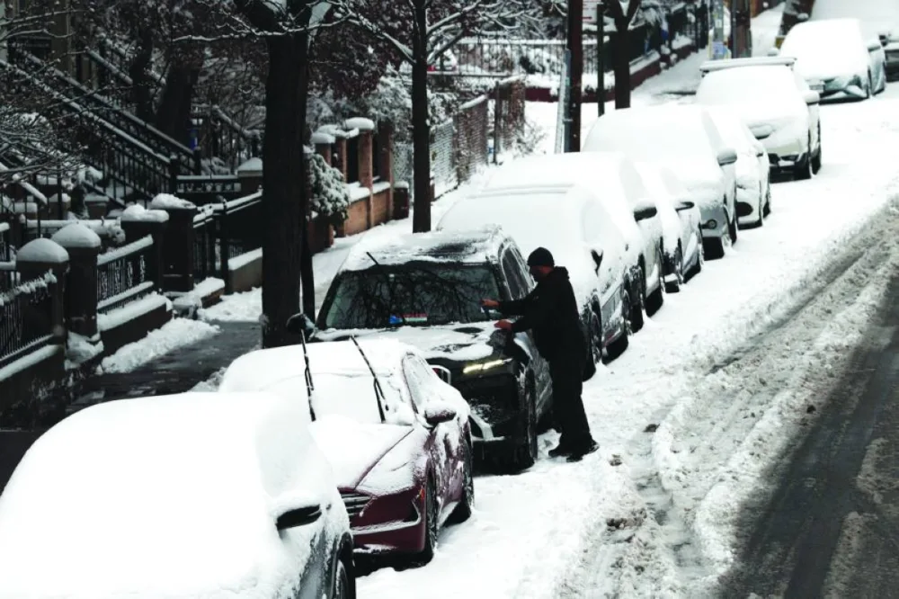 A man cleans off his car of snow in Brooklyn after an overnight storm, in New York City, Saturday.