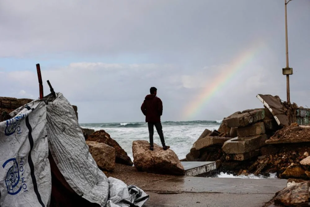 TOPSHOT - A displaced Palestinian man stands outside the family tent shelter erected in the harbour, as he looks at a rainbow out at sea, as the region experiences rain and cold winter conditions, in Gaza City an December 28, 2025. The majority of Gaza's 2.4 million people have been displaced, often multiple times, by the war that began with Hamas's attack on southern Israel on October 7, 2023. With many displaced living in tent camps, raising serious concerns over winter. (AFP)