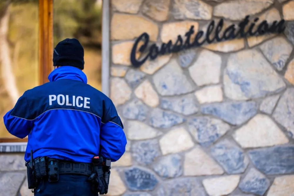 A police officers stands at the entrance of the building Constellation, housing the bar Le Constellation following an explosion that ripped the venue in Crans-Montana, in January 1, 2026 during New Year's Eve celebrations. Several dozen people are presumed dead and around 100 injured after a fire ripped through a crowded bar in the luxury Swiss ski resort town of Crans-Montana, police said early January 1, 2026. (Photo by MAXIME SCHMID / AFP)