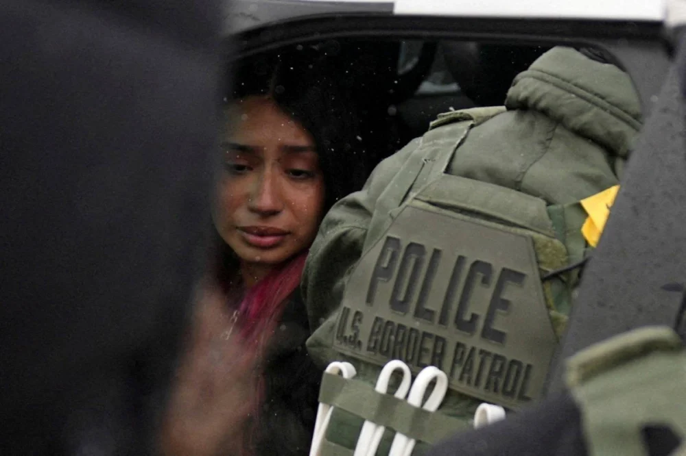 A detained woman sits inside a vehicle surrounded by federal agents, as immigration enforcement continues in Minneapolis. – Reuters
