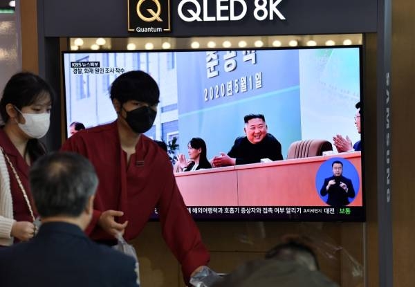 أناس يمرون أمام شاشة إخبارية تليفزيونية تظهر صورة الزعيم الكوري الشمالي كيم جونج أون وهو يحضر احتفالًا بمناسبة الانتهاء من مصنع سمادون للأسمدة الفوسفاتية (أ ف ب)