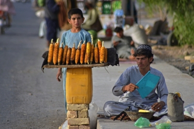 A vendor (R) selling corns waits for customers along the roadside in Kandahar on October 2, 2021. (Photo by Javed TANVEER / AFP)