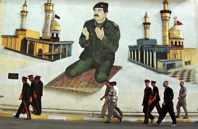 Iraqis pass a mural showing President Saddam Hussein praying in front of Iraq's two main Shiite Muslim mosques of Karbala near the Iraqi-Iranian border point of al-Munziriya, 190 kms northeast of Baghdad, 09 April 2000. Hunderds of Iranian pilgrims cross into Iraq every day to visit Shiite holy sites in the south of the country. Shiites make up the majority of Iraq's predominantly Muslim population, but the Iraqi president is a Sunni Muslim. (Photo by Karim SAHIB / AFP)