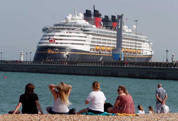 People enjoy the hot weather on the beach as the cruise ship «Disney Magic» ferry is seen docked in the port of Dover, amid the coronavirus disease (COVID-19) outbreak, in Dover, Britain August 9, 2020. REUTERS/Paul Childs